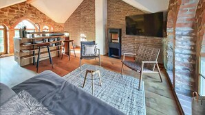 Ein Loft-Zimmer mit Kamin, Wand-Fernseher, Küchenzeile mit integriertem Regal und einer gemütlichen Sitzecke mit Teppich.
