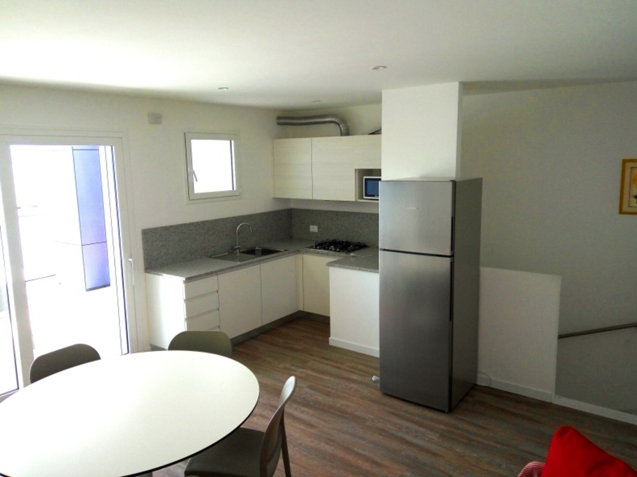 A compact kitchen with white cabinets, a stainless steel refrigerator, a sink, and a small window.
