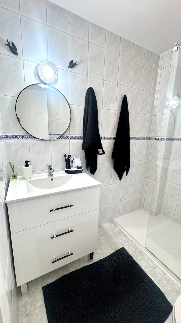 A bathroom with a white sink, mirror, and black towel hanging on the wall.