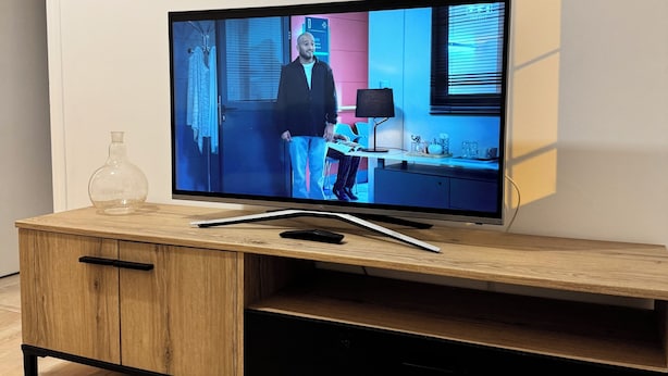 A flat-screen TV on a wooden TV stand with a laptop and a glass vase.