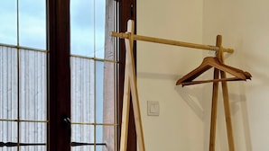 A room with a wooden bed, a wooden clothes rack, and a window with a view of a building.