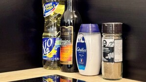 A kitchen counter with various bottles and containers, including a bottle of Graines d'Orme 3, a bottle of Vinaigre Blanc, a jar of Cerebos, and a container of black pepper.