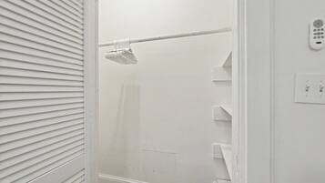 A white bathroom with a shower, a towel rack, and a wall-mounted control panel.