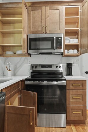 A kitchen with wooden cabinets, a microwave, a stove, and a coffee maker.