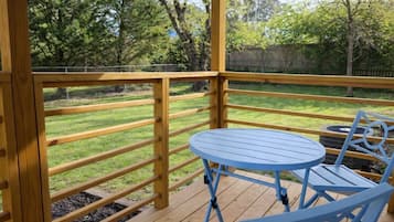 A wooden deck with a blue table and chairs, surrounded by a wooden railing and a grassy yard.