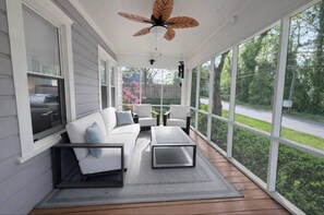 A covered porch with a white sofa, two armchairs, a coffee table, and a ceiling fan.