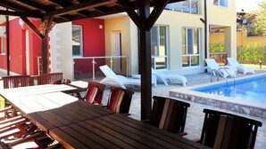 A covered outdoor area with a pool, lounge chairs, and a wooden table. - BLUE PEARL 2-BEDROOM LUXURY MAISONETTE IN PANORAMIC ROOF COMPLEX (Balchik)