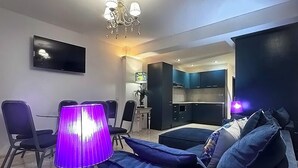 A modern living room with a sofa, a purple lamp, a TV, and a chandelier. - BLUE PEARL 2-BEDROOM LUXURY MAISONETTE IN PANORAMIC ROOF COMPLEX (Balchik)