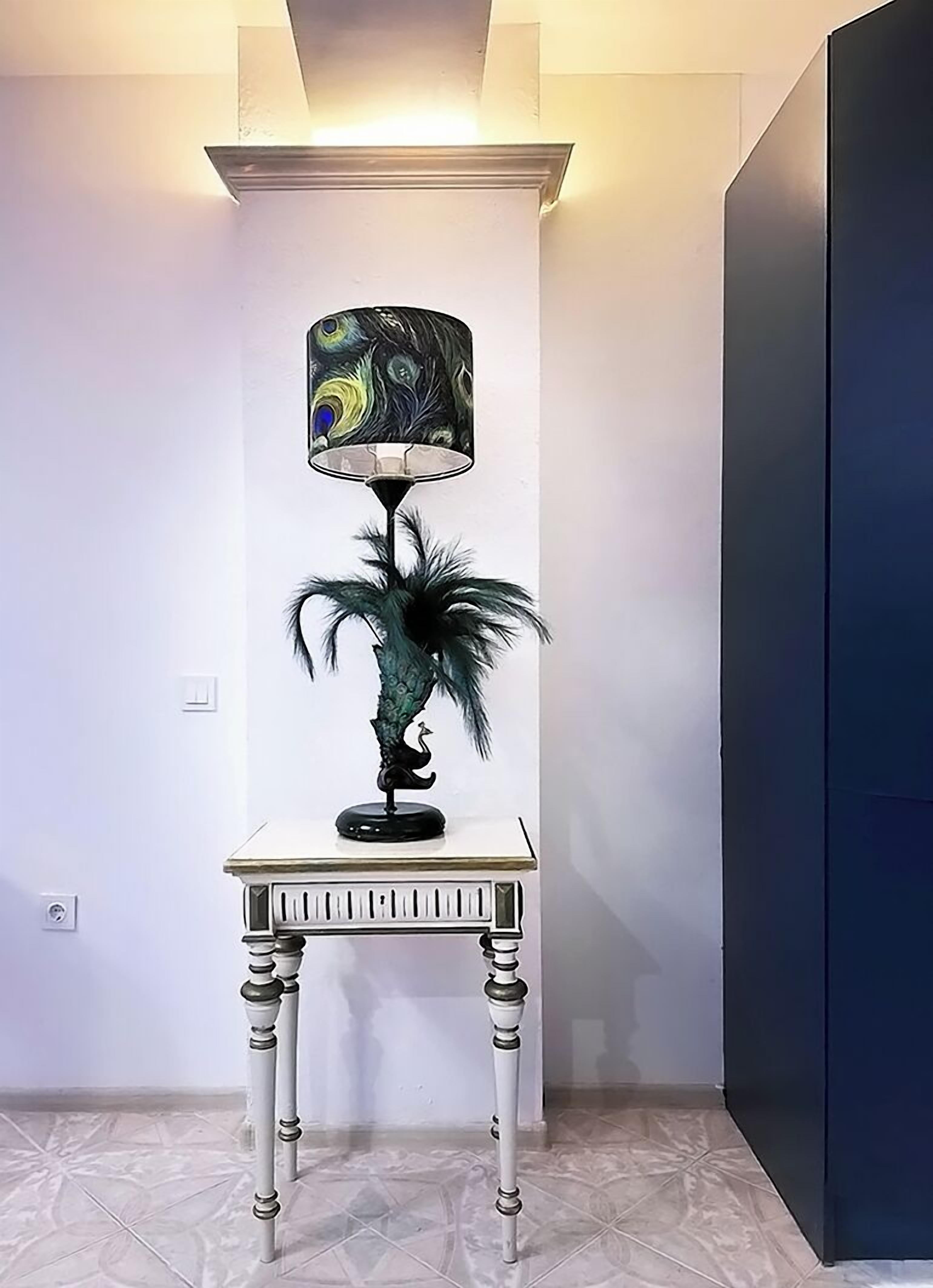 Et hjørne med et hvidt bord, en dekorativ lampe med påfugl-design og et mørkt skab.