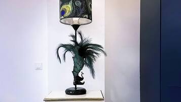 Een hoek met een witte tafel, een decoratieve lamp met pauwenmotief en een donker kastje.