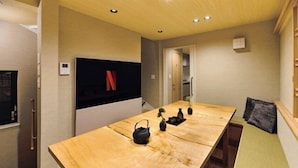 Een moderne woonkamer met een lange houten tafel, een flatscreen televisie en een minimalistische inrichting.