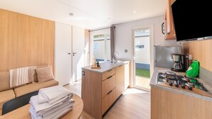 A compact kitchen with a central island, a dining area with a sofa, and a TV mounted on the wall. - Premium Caravan in Erezee With Terrace (Erezee)