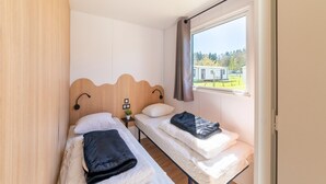 A room with two single beds, a small table with a plant, and a window with a view of a building. - Premium Caravan in Erezee With Terrace (Erezee)