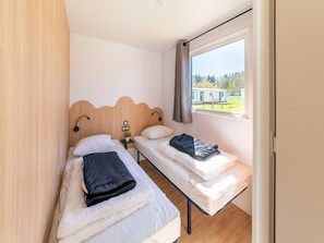 A room with two single beds, a small table with a plant, and a window with a view of a building. - Premium Caravan in Erezee With Terrace (Erezee)