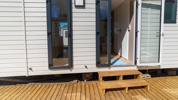 A mobile home with two open doors revealing interior spaces, a wooden deck, and a small bench. - Premium Caravan in Erezee With Terrace (Erezee)