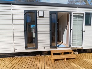 A mobile home with two open doors revealing interior spaces, a wooden deck, and a small bench. - Premium Caravan in Erezee With Terrace (Erezee)