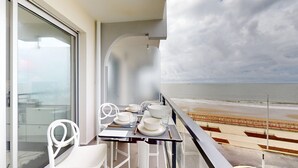 Een balkon met een eettafel, met uitzicht op een strand.