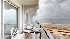 Ein Balkon mit Esstisch, der auf einen Strand blickt.
