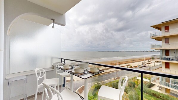 A balcony with a table set for dining, overlooking a beach and a residential area. - Belle Isle - Breathtaking Ocean Views (La Baule-Escoublac)