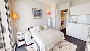 Een moderne hotelkamer met een bed, nachtkastje, lamp, kunstwerk, kledingkast en kitchenette.