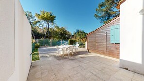 A patio with a table and chairs, a wooden shed, and a chain-link fence. - Villa Aquatica (Saint-Hilaire-de-Riez)