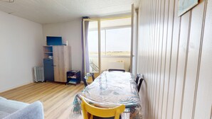 Una habitación con suelo de madera, una mesa con sillas, un radiador, un armario y una ventana con cortinas.