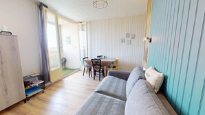 Una sala de estar acogedora con un sofá, una mesa de comedor con sillas, una pequeña cocina y un ventanal corredero que da a un espacio exterior.