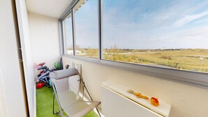Un balcón con vista a un paisaje rural, una silla, una mesa con un juguete y una bicicleta.