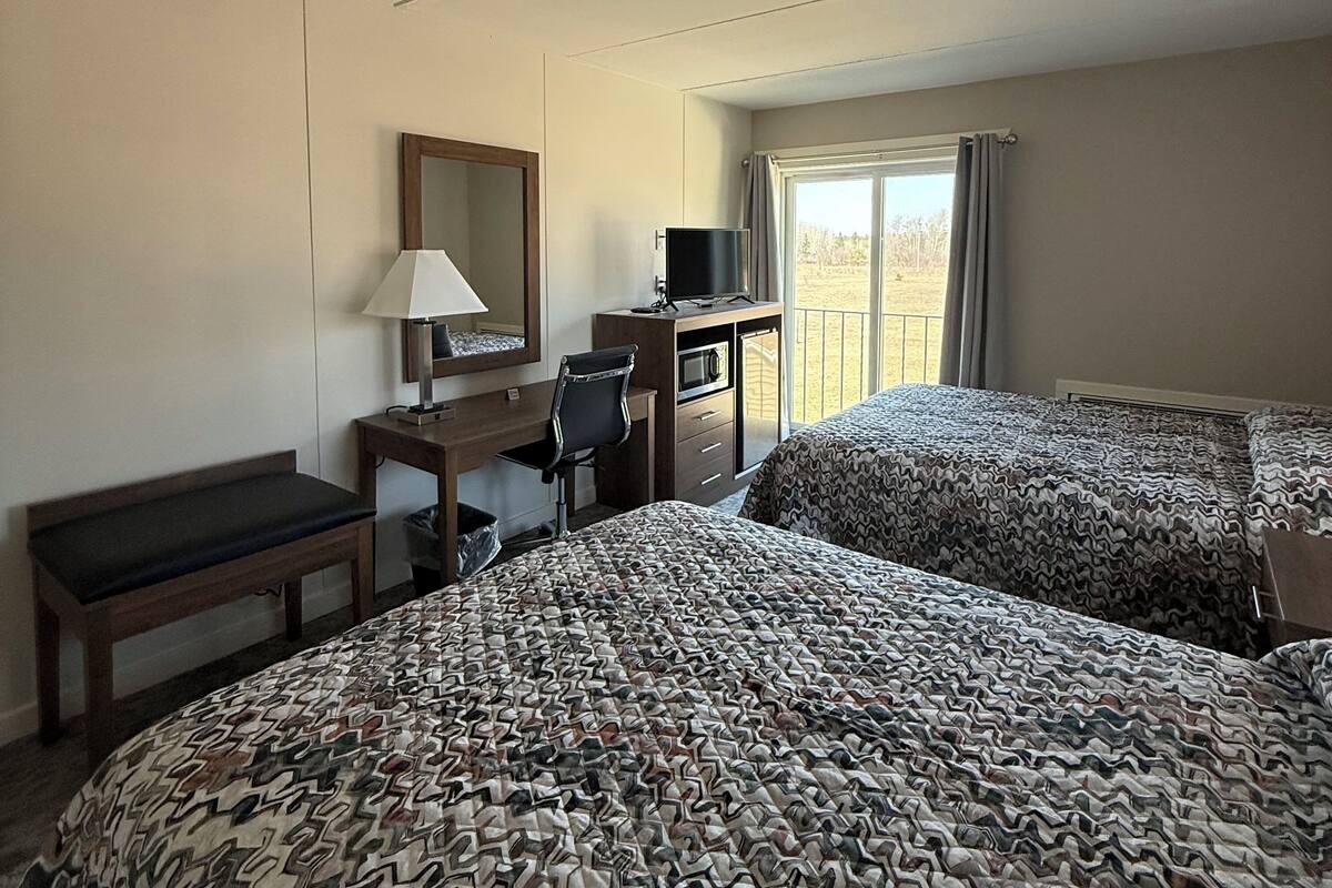 A hotel room with two beds, a desk with a chair, a TV, and a window with curtains.
