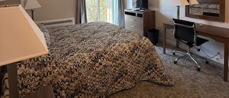 Habitación de hotel con cama, escritorio, silla, televisor y un espejo grande.