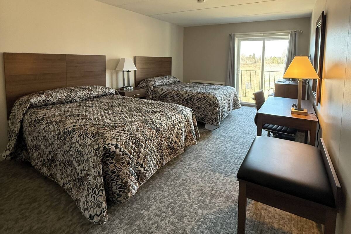 A hotel room with two beds, a desk, a chair, and a window with a view.