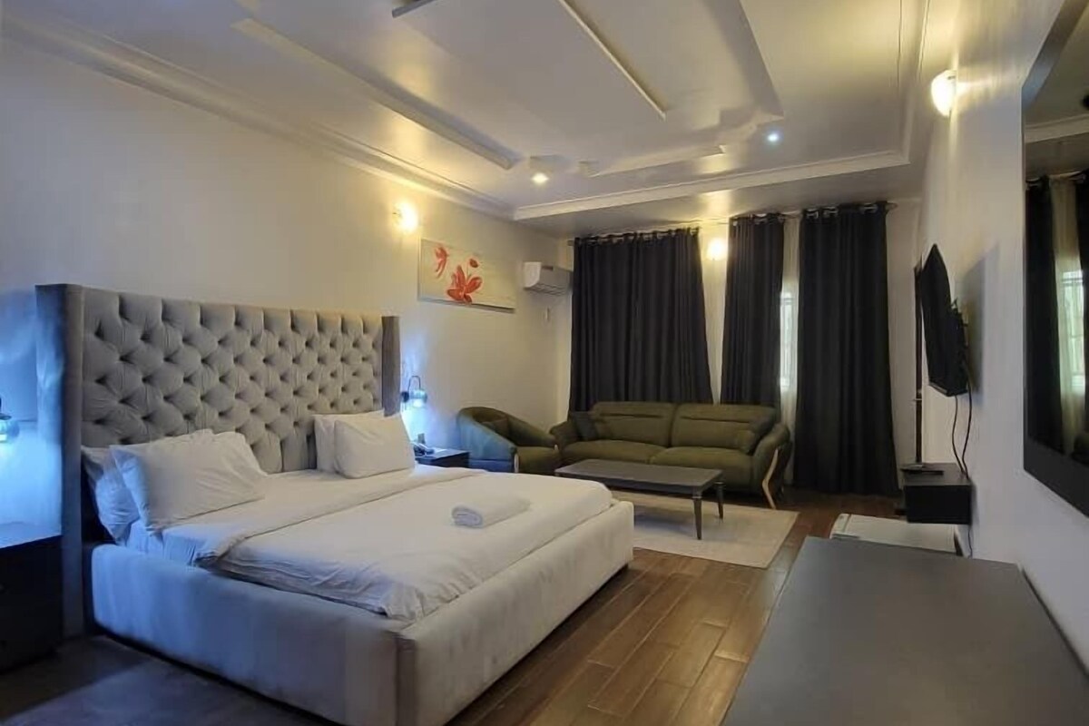 Una habitación de hotel moderna con una cama grande, un sofá, una mesita y un televisor.