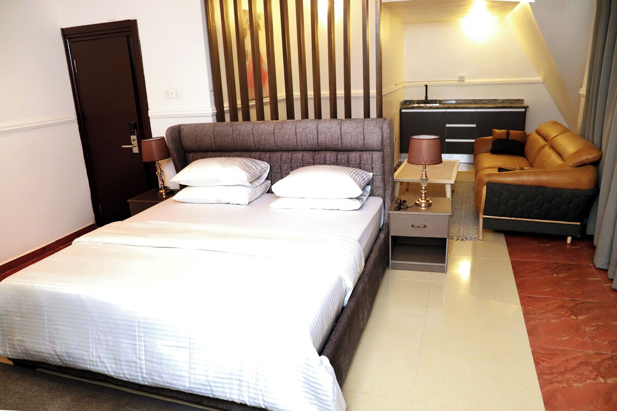 Una habitación de hotel con cama, mesitas de noche, cómoda, sofá y cortina.