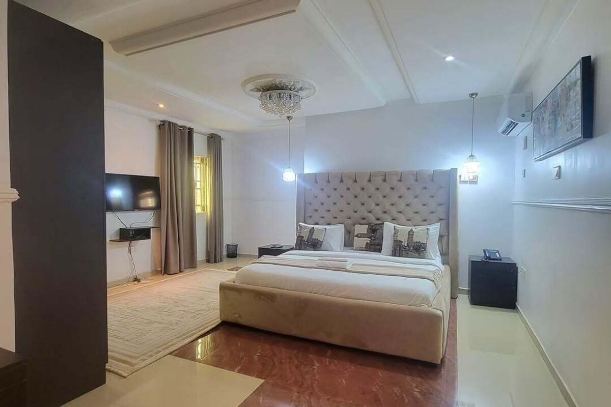 Una habitación de hotel moderna con una cama grande, un televisor de pantalla plana, una araña y un espejo amplio.