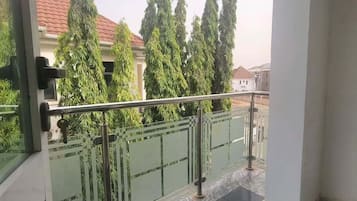 A balcony with a glass railing, a view of trees, and a tiled floor.