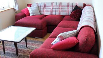 A red sectional sofa with a glass coffee table, patterned rug, and a plaid throw blanket.