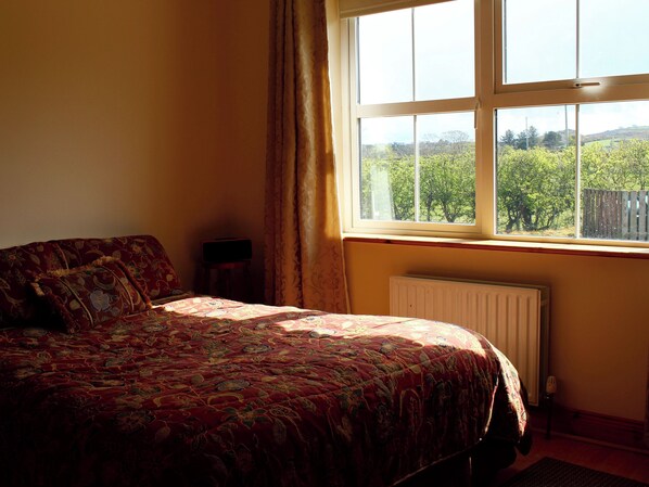 Quarto com cama grande, janela com vista para área verde e radiador.