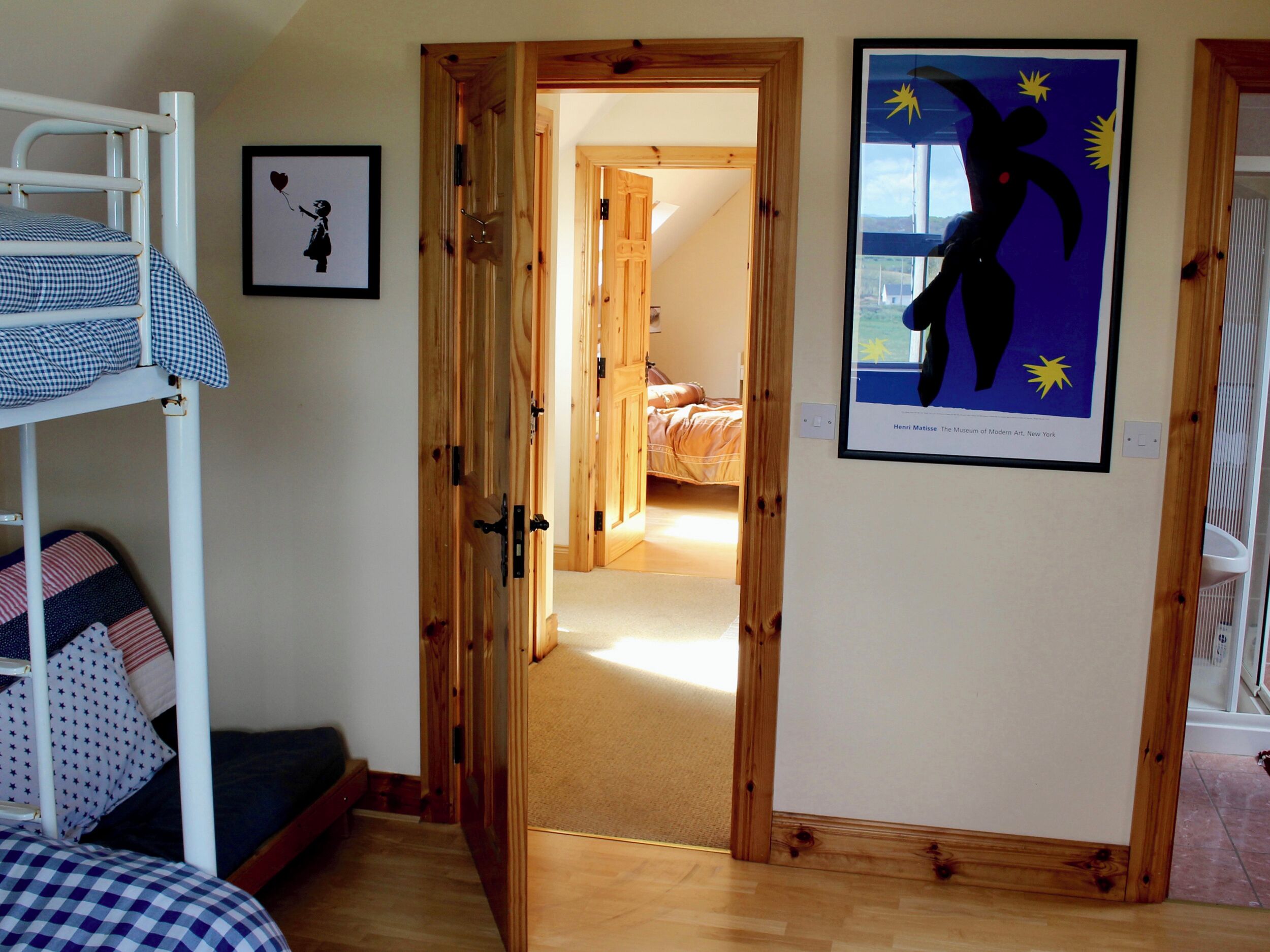 Una habitación con una cama litera, una puerta de madera que da a otra habitación y una obra de arte enmarcada en la pared.