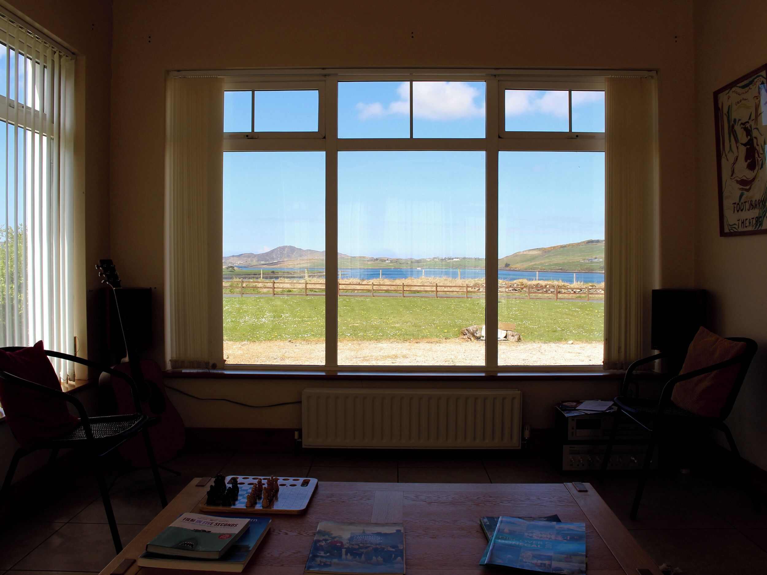 Ein Zimmer mit großem Fenster, Heizkörper, Tisch mit Büchern und zwei Stühlen.