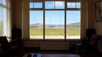 Ein Zimmer mit großem Fenster, Heizkörper, Tisch mit Büchern und zwei Stühlen.