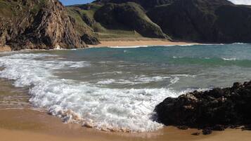 A beach with waves, rocky cliffs, and a clear sky.