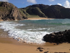 Uma praia com ondas, falésias rochosas e céu claro.