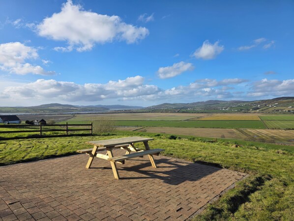 Una mesa de picnic en un área con césped, con vista a campos y colinas distantes.