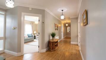 A hallway with wooden flooring, a potted plant, a wooden side table, and a framed picture on the wall.