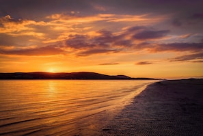 Una playa con un atardecer, agua tranquila y colinas al fondo.