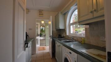 A compact kitchen with a washing machine, a sink, and a window overlooking a garden.