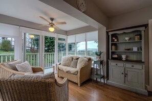 A sunlit room with a wicker sofa, a ceiling fan, and a view of greenery outside.