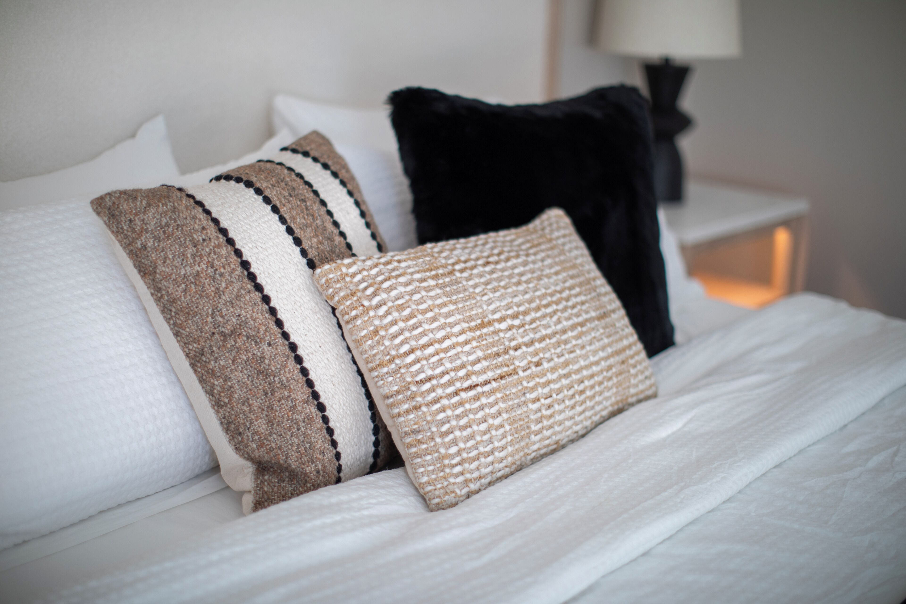 A bed with multiple pillows and a bedside table with a lamp.