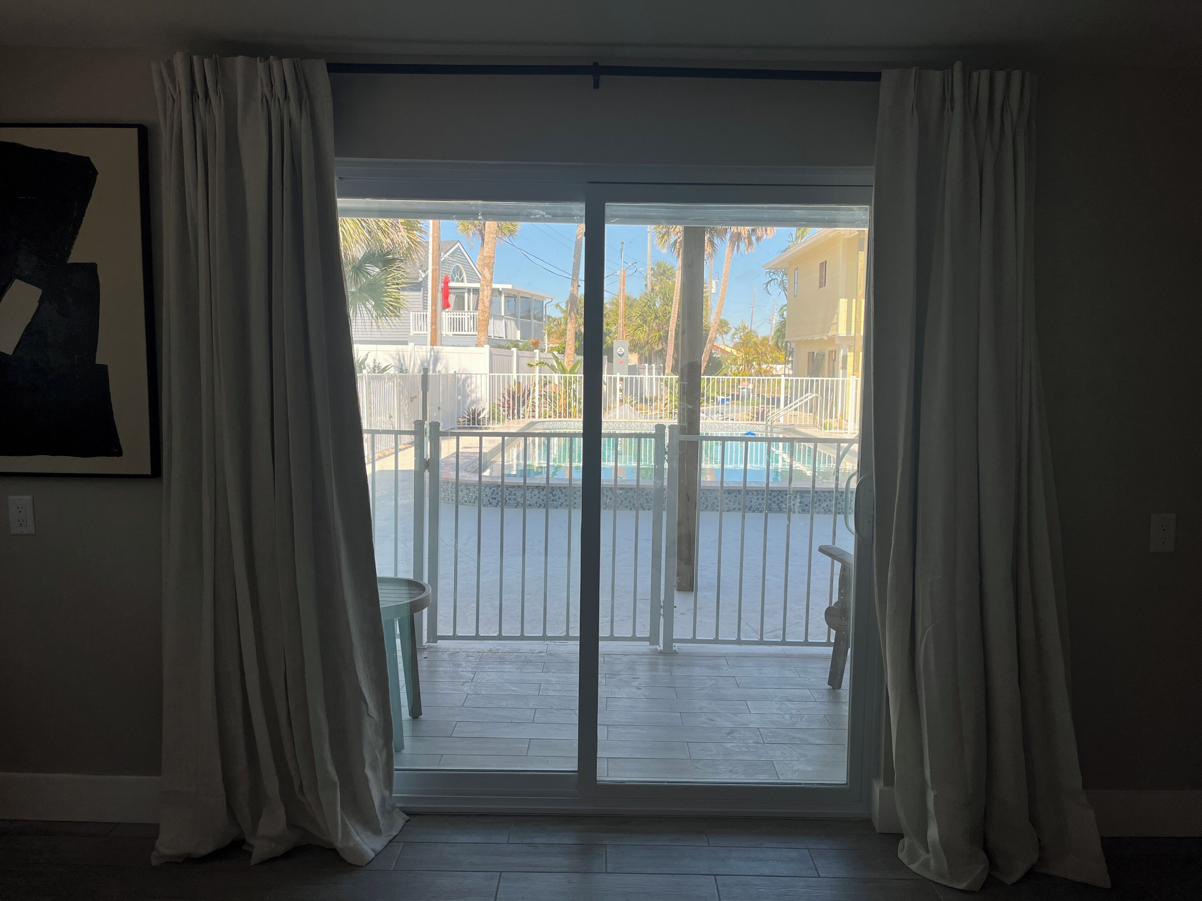 Ein Zimmer mit einer Glastür, die zu einem Außenbereich mit Pool und weißem Zaun führt.