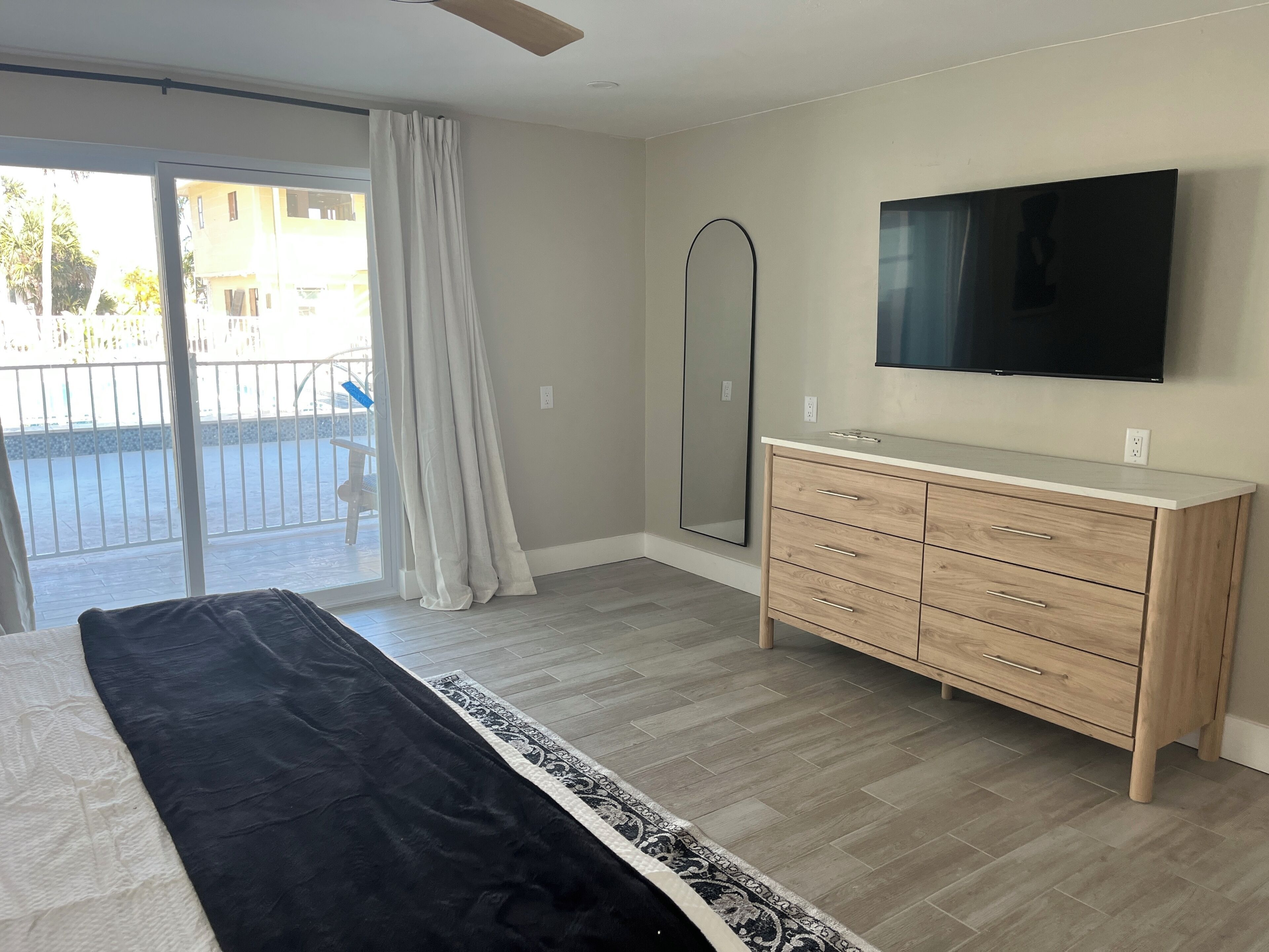 Quarto com cama, cômoda, televisão e porta de vidro corrediça que dá para uma varanda.